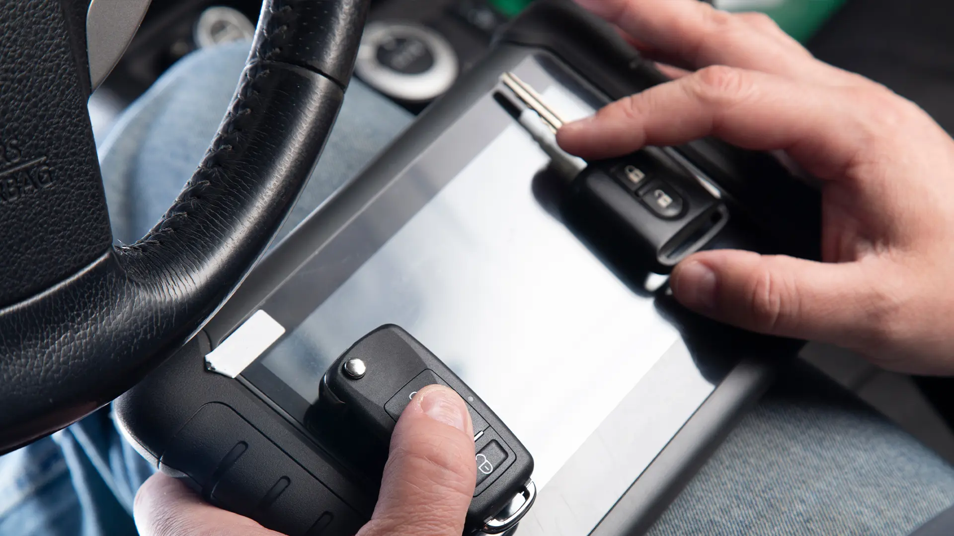 A close-up of our locksmith's hands holding a client’s car key, a freshly cut duplicate, and a portable tablet we use to program fobs.