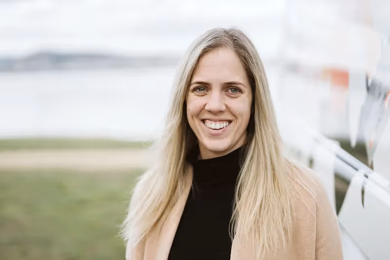 Smiling woman with long blonde hair in black top and beige coat outdoors