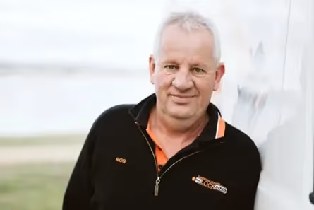 Smiling middle-aged man in black jacket outdoors on a light background