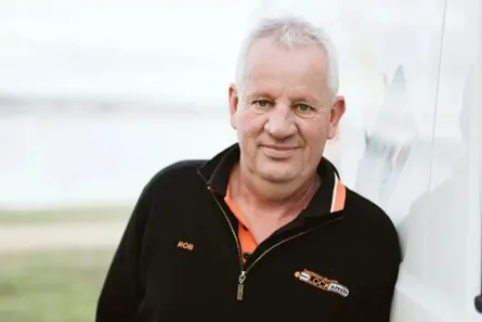 Smiling middle-aged man in black jacket outdoors on a light background