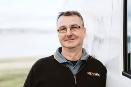 Smiling middle-aged man in glasses and black jacket standing outdoors