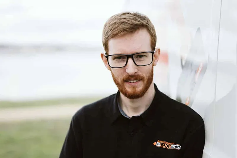 Smiling man with red beard and glasses wearing black polo shirt