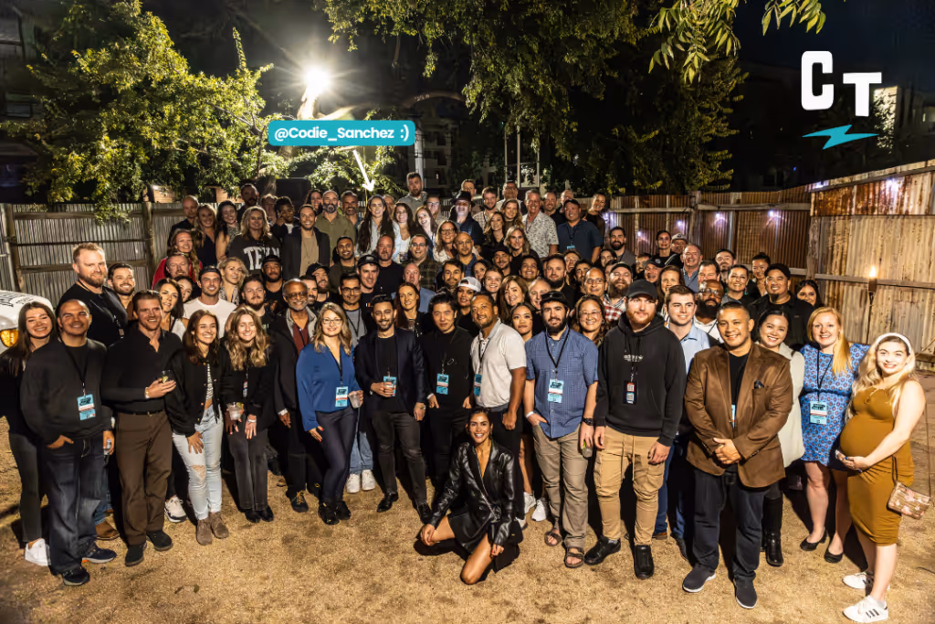 A large group of people posing outdoors in a backyard setting, with some smiling and a tag pointing to one individual. The caption reads, "We’re never doing this again…" as laughter echoes through the crisp air.