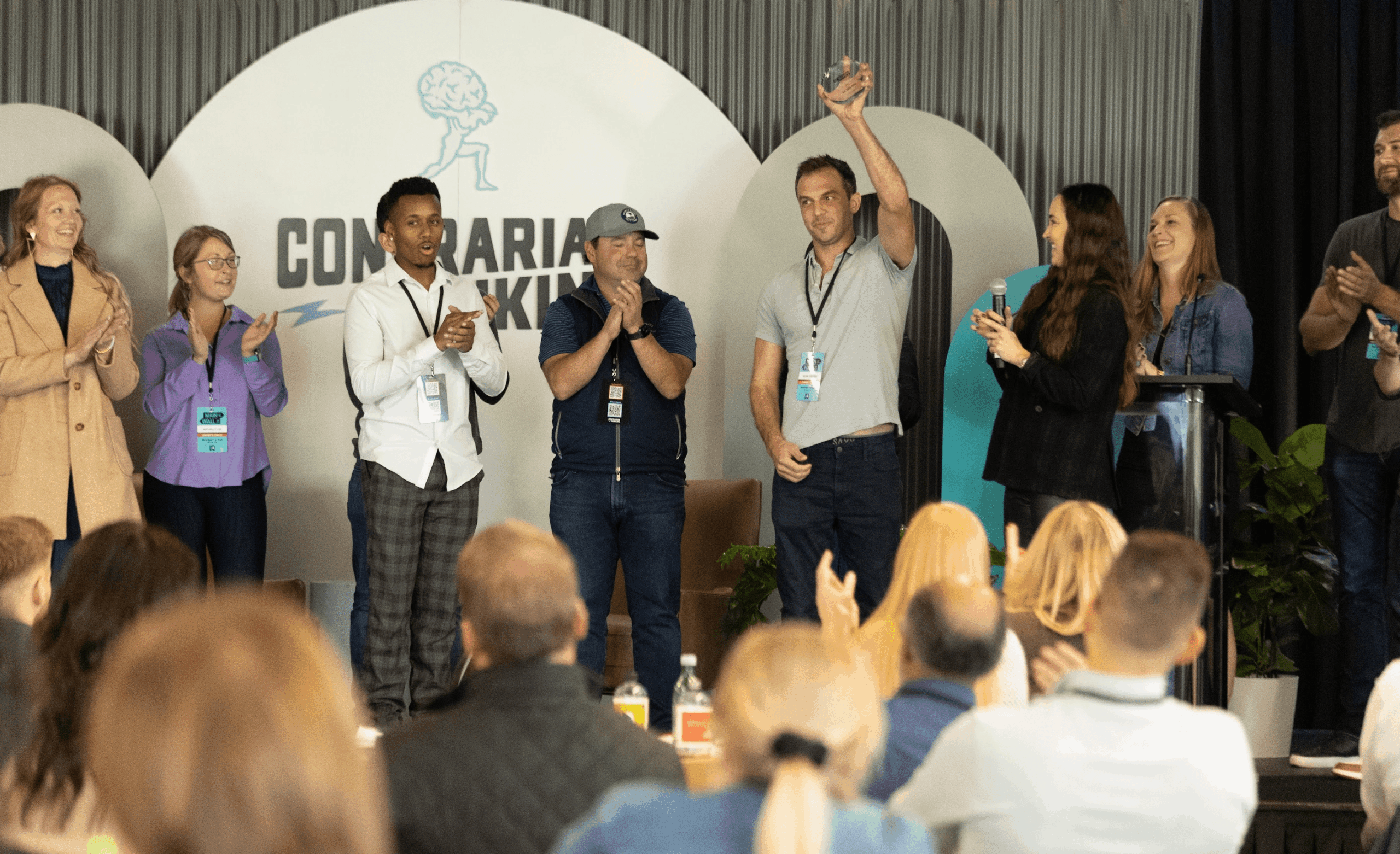 Group of Contrarian Thinking community members on stage at an event, applauding a man holding up an award.