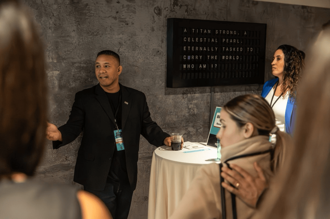 A man in a black suit leads a conversation at a Contrarian Community event, engaging with attendees.