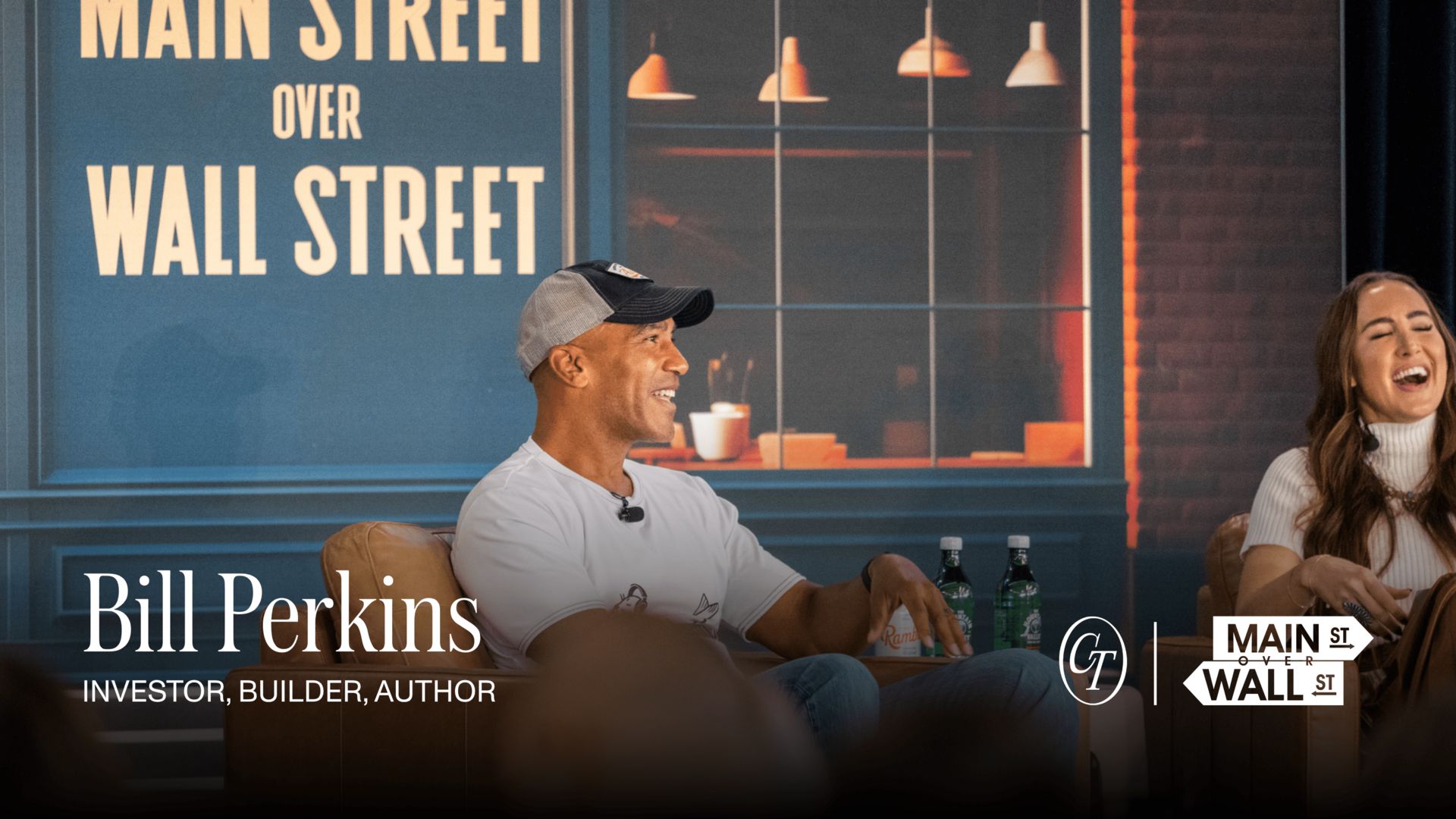 Bill Perkins smiling while speaking onstage at a Main Street Over Wall Street event, labeled as investor, builder, and author, with event branding behind him.