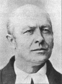 Black and white headshot of a middle-aged man with a receding hairline, wearing a dark jacket and white shirt collar.