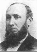 Black and white portrait of a man with a full beard wearing a jacket and shirt, looking slightly to the side.