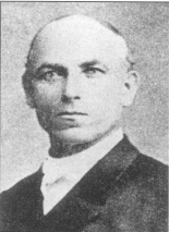 Black and white portrait of a man in formal early 20th-century attire with a serious expression.