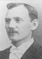 Black and white portrait of a man with a mustache, short hair, wearing a suit jacket, white shirt, and bow tie.
