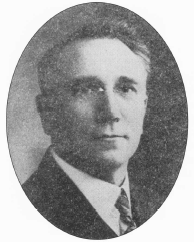 Black and white oval portrait of a man wearing a suit and tie, facing slightly left with short hair neatly combed.