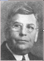 Black and white portrait of a man wearing glasses and a suit, looking slightly to the right of the camera.