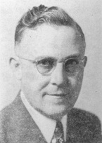 Black and white photo of a middle-aged man wearing glasses, a suit, and a tie, smiling slightly with neatly combed hair.