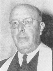 Black and white portrait of a bald man wearing round glasses, a collared shirt, and a suit with a clerical collar and a stole.