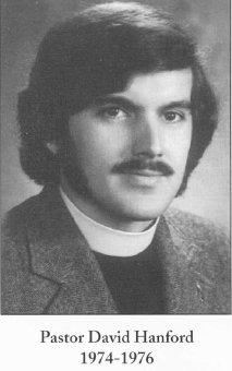 Black and white portrait of a man with dark hair and a mustache wearing a clerical collar and jacket.