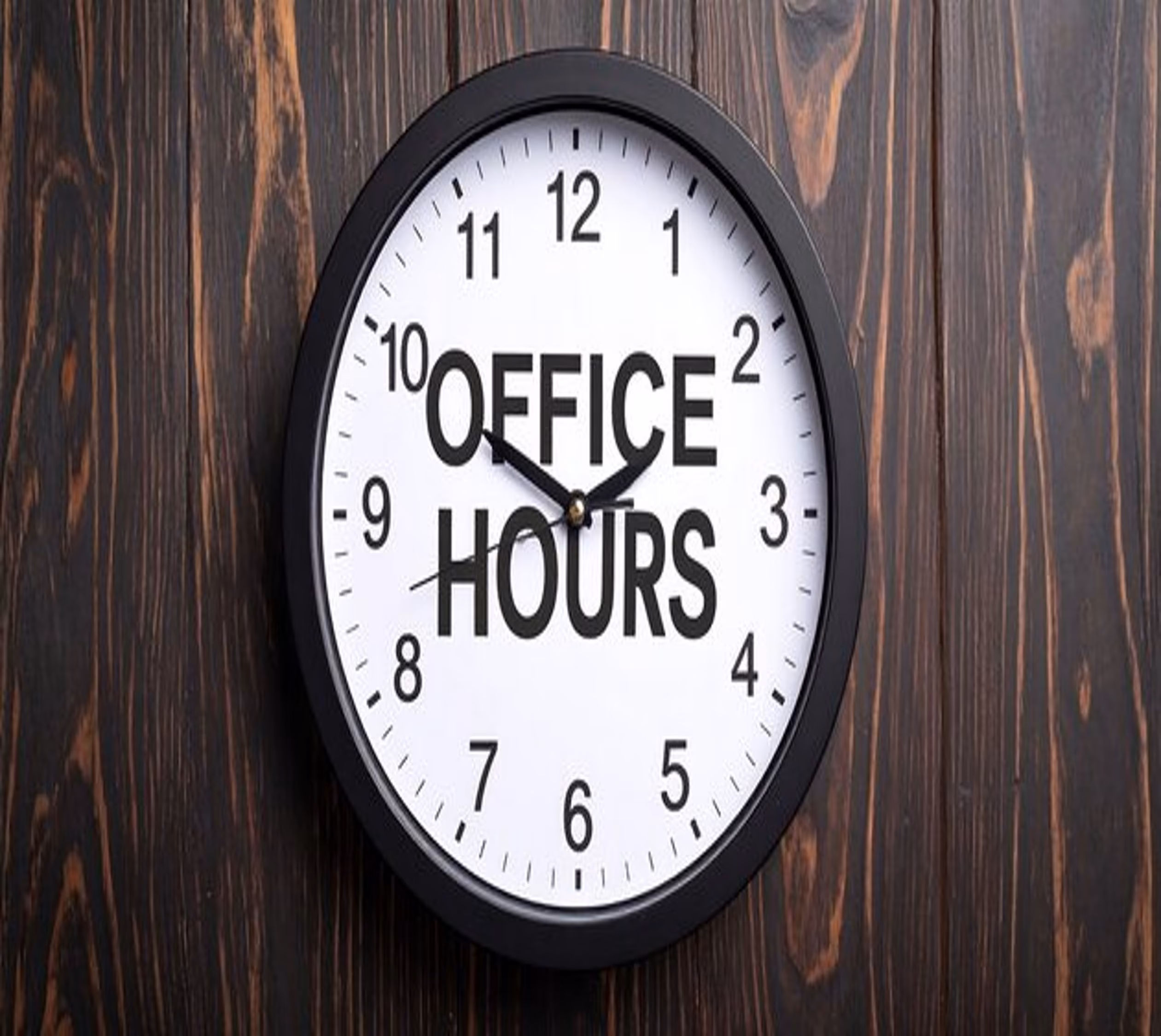 A black-framed wall clock with white face showing the time at 10:10, with the words OFFICE HOURS in bold black letters across the center, mounted on a dark wood-paneled wall.