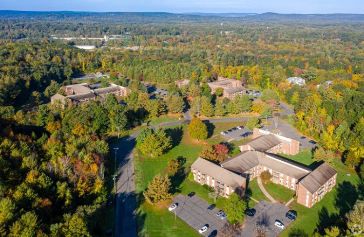 Aerial view of a suburban area with several brick apartment buildings surrounded by dense, colorful autumn trees and multiple parking lots.
