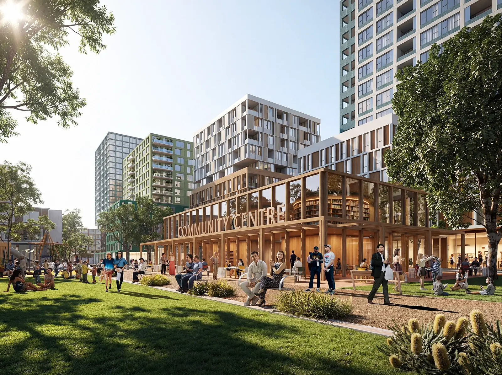The image shows a vibrant urban park scene with people relaxing, walking, and socialising on a grassy area in front of a modern, glass-walled community centre. Surrounding the park are several tall, contemporary apartment buildings with a mix of green and white facades. Trees and landscaped plants add greenery, and the atmosphere is bright and welcoming, suggesting a lively community space.