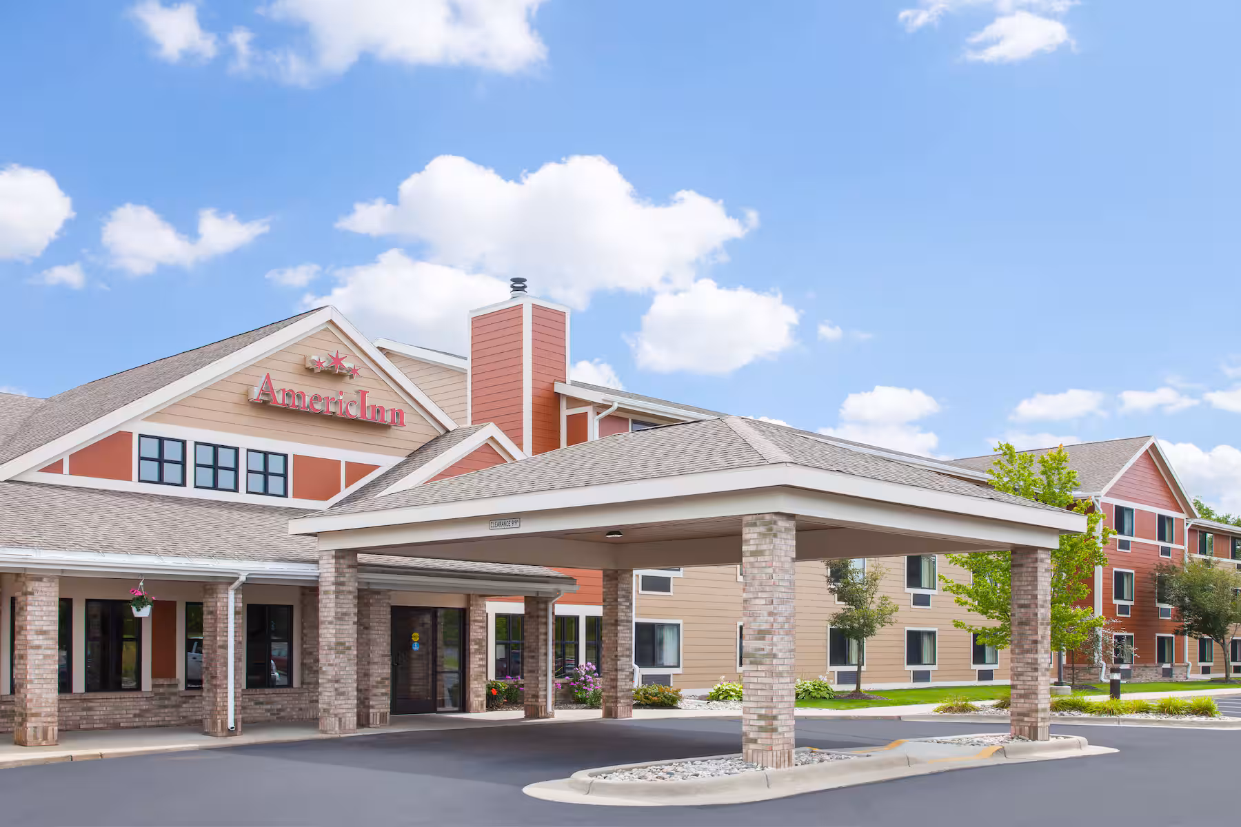 AmericInn hotel exterior with covered driveway entrance under a clear blue sky.