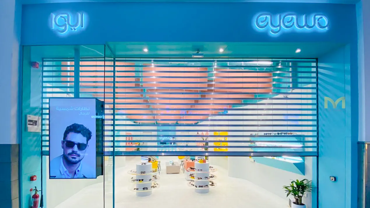 Modern eyewo retail store with blue theme and shutter partially closed showing sunglasses displays inside.