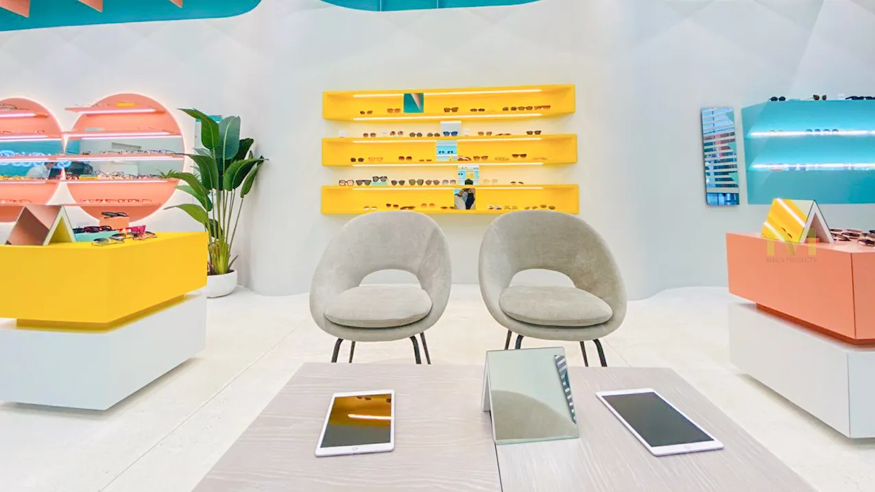 Modern eyewear store with yellow and teal displays, two gray chairs, tablets, and a mirror on a table.