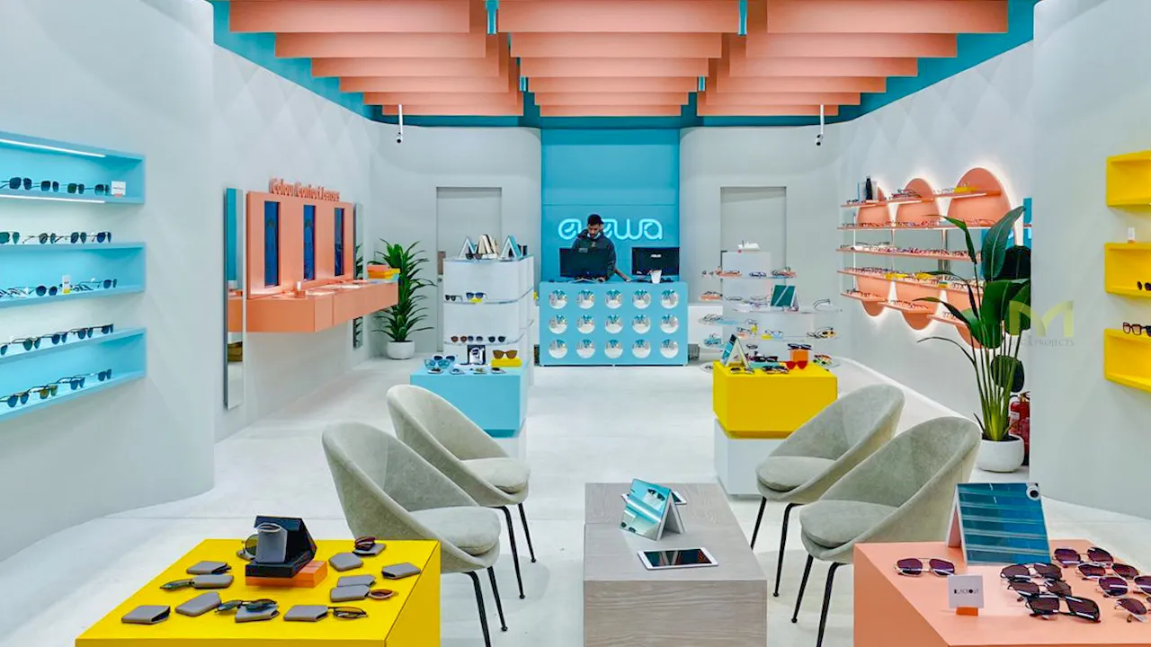Bright eyeglass store interior with colorful displays, seating, and a staff member behind the counter.