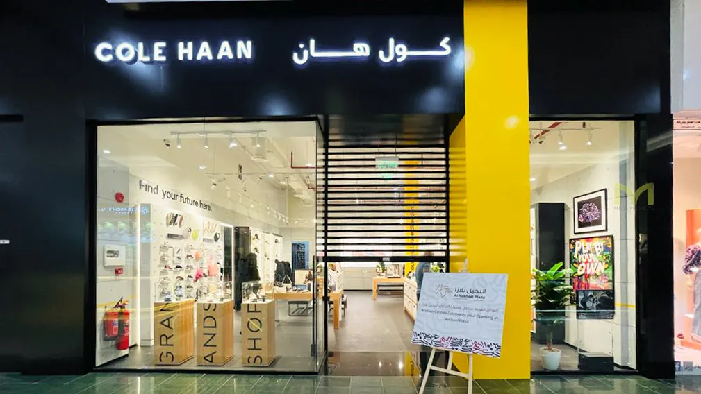 Front view of Cole Haan store with glass doors and illuminated signage in a mall.