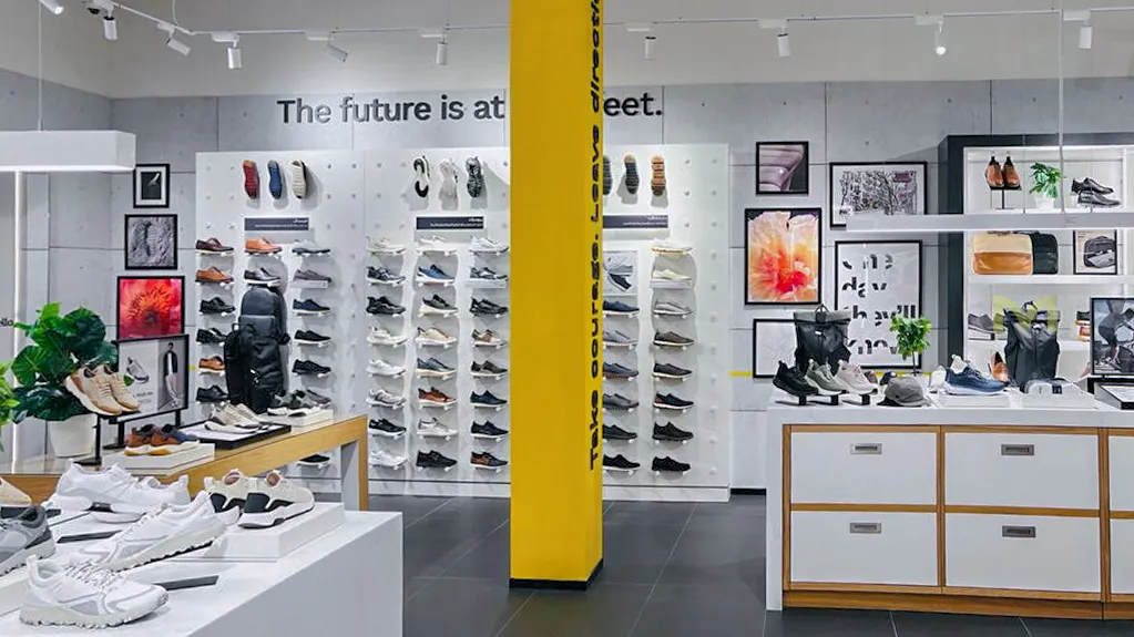 Modern retail shoe store with white walls, sneakers on shelves, and a yellow pillar with text.
