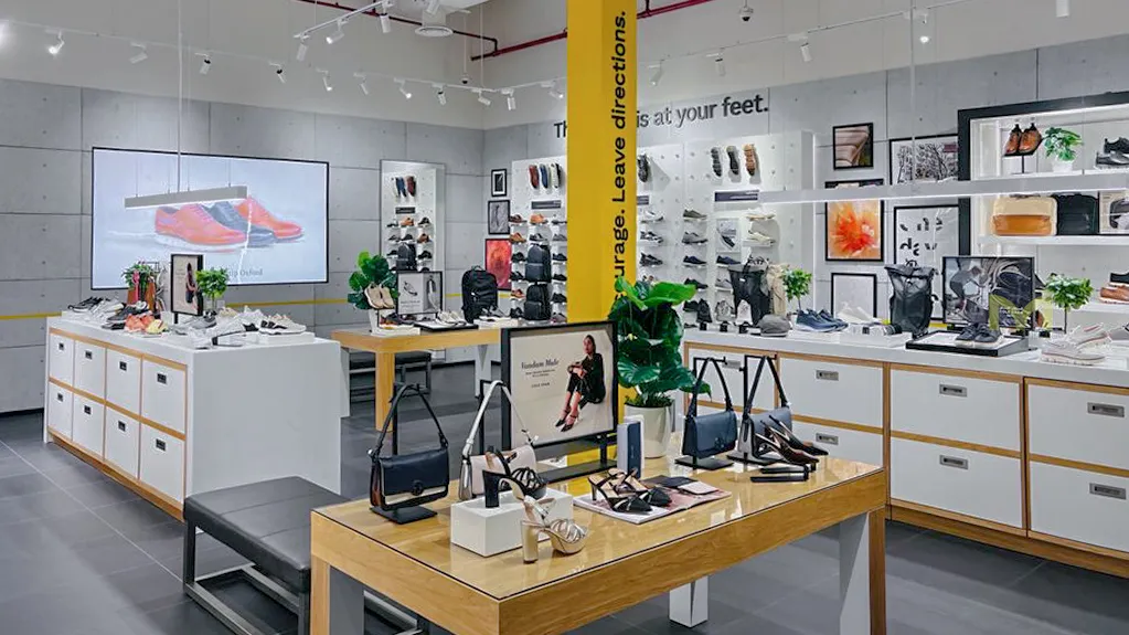 Modern retail store interior with shoes, handbags, plants, and framed artwork on display shelves.