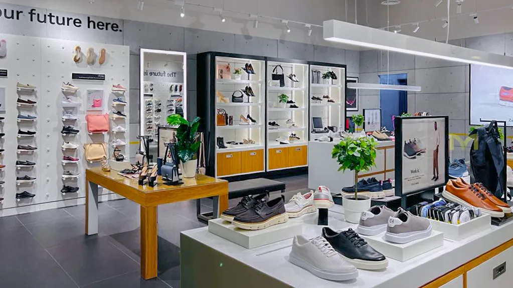 Modern retail store interior displaying various shoes, handbags, and plants on shelves and tables.