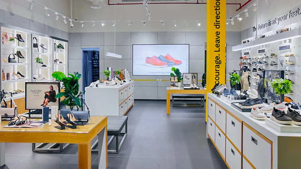 Modern shoe store interior with displays holding shoes, handbags, and potted plants under bright lighting.