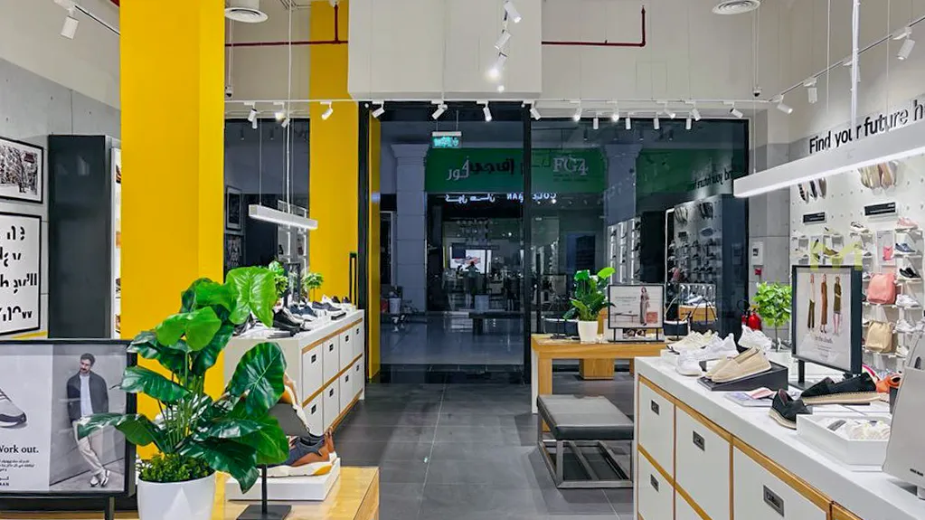 Bright modern shoe store interior with white shelves, yellow pillars, and green potted plants.