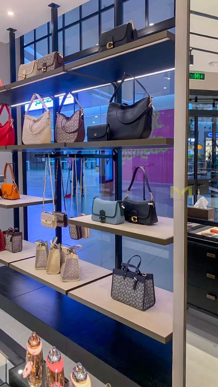 Shelves displaying various luxury handbags in a retail store with glass walls and bright lighting.
