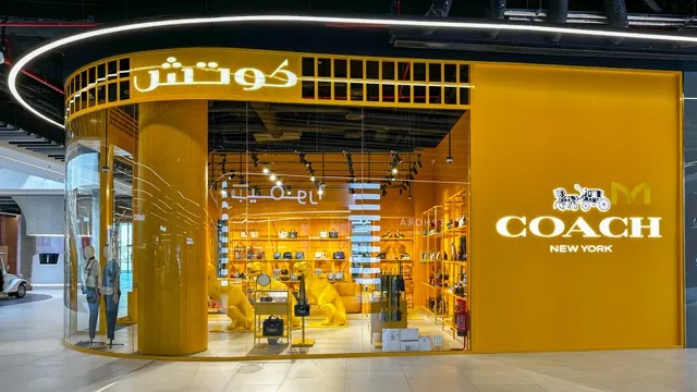 Coach New York retail store with bright yellow facade and handbags displayed inside.
