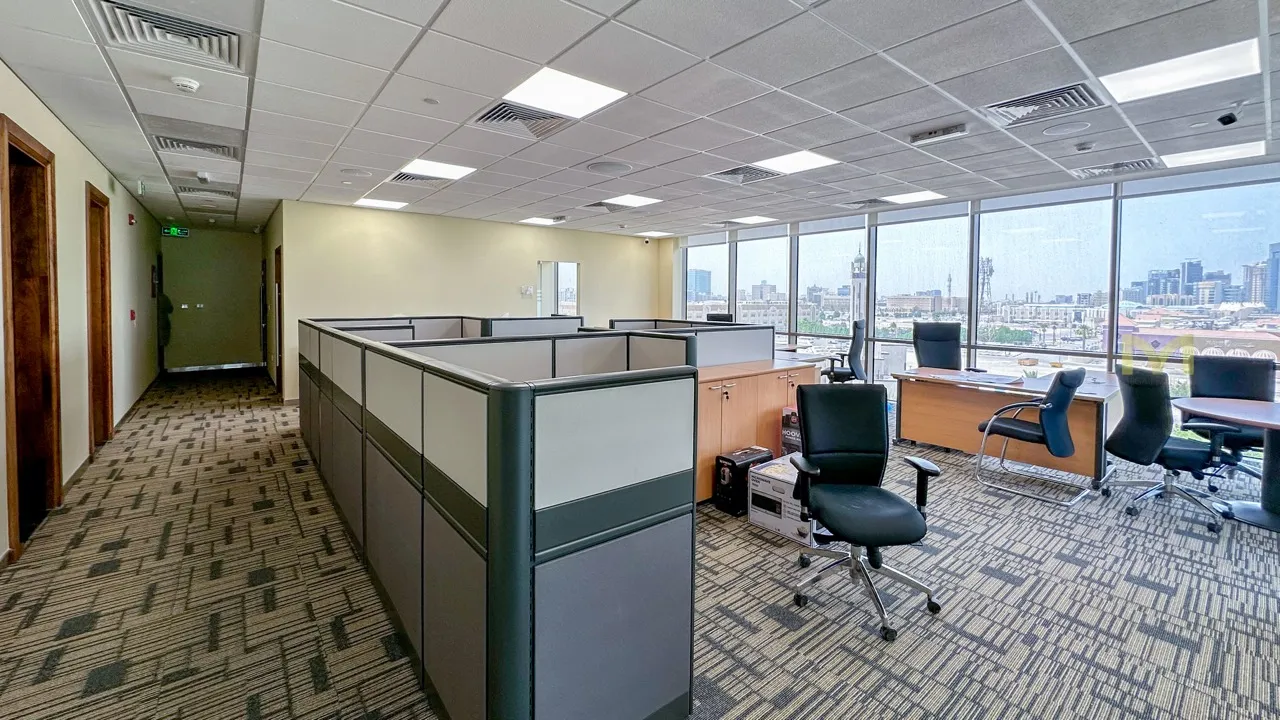 Modern office with cubicles, desks, chairs, and large windows overlooking a cityscape.