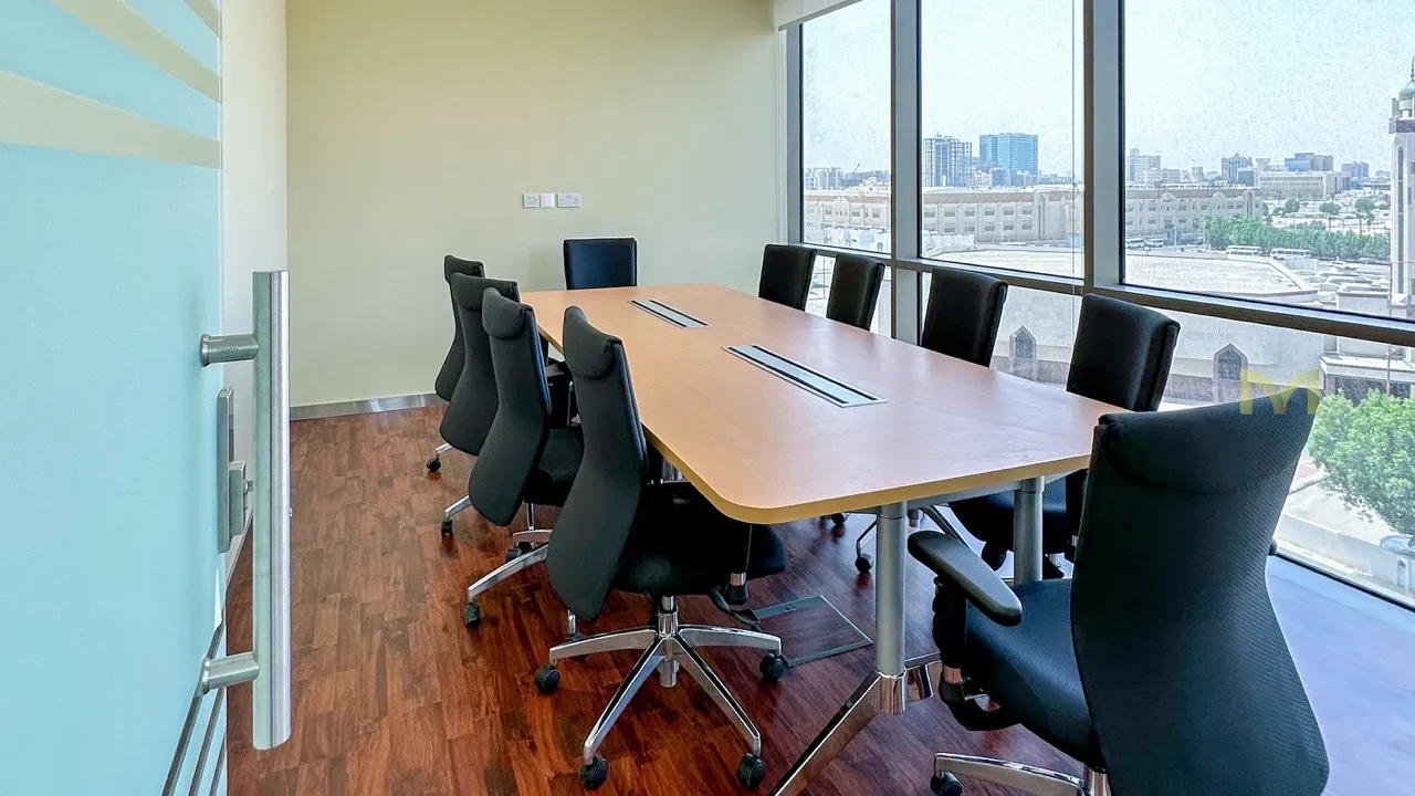 Modern conference room with wooden table, black office chairs, and large windows showing city view.
