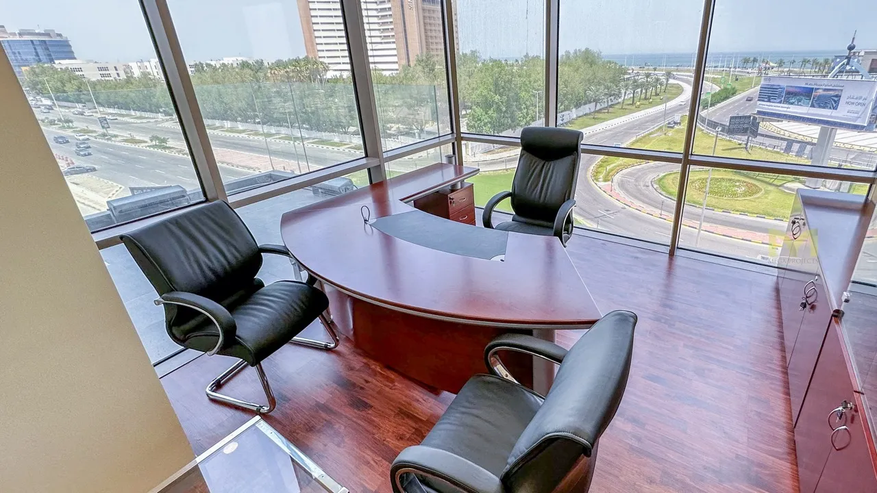 Modern office with a curved wooden desk, three black leather chairs, and floor-to-ceiling windows.