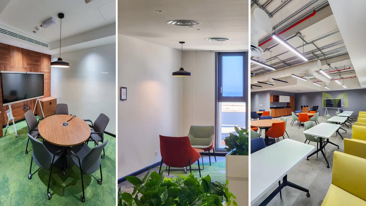 Modern office with a meeting room, seating area with plants, and a workspace with colorful chairs.
