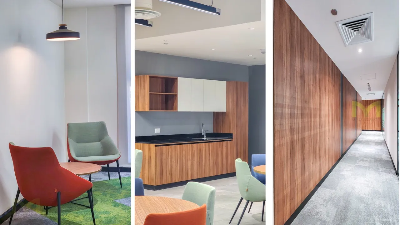 Modern office lounge and kitchenette with green and orange chairs, wood cabinets, and a wood-paneled hallway.