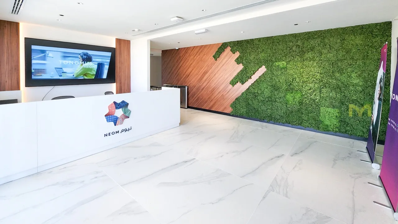 Modern lobby with white marble flooring, a white reception desk, green moss wall, and wood paneling.