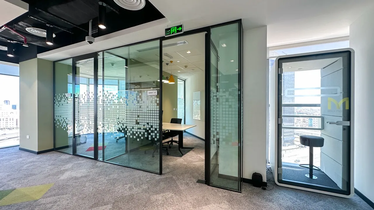 Modern office space with glass meeting room and a soundproof pod with a stool inside.