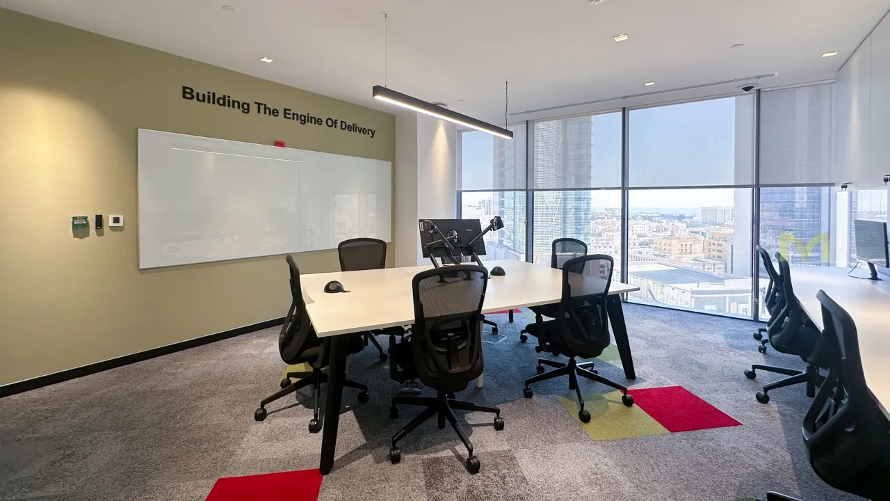 Modern office room with a large table, black chairs, whiteboard, and city view through windows.