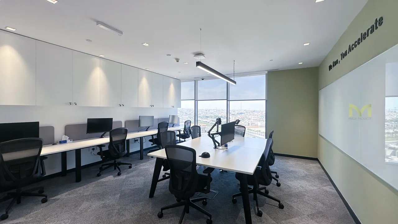 Modern office with white desks, black chairs, computer monitors, and large windows overlooking a city.