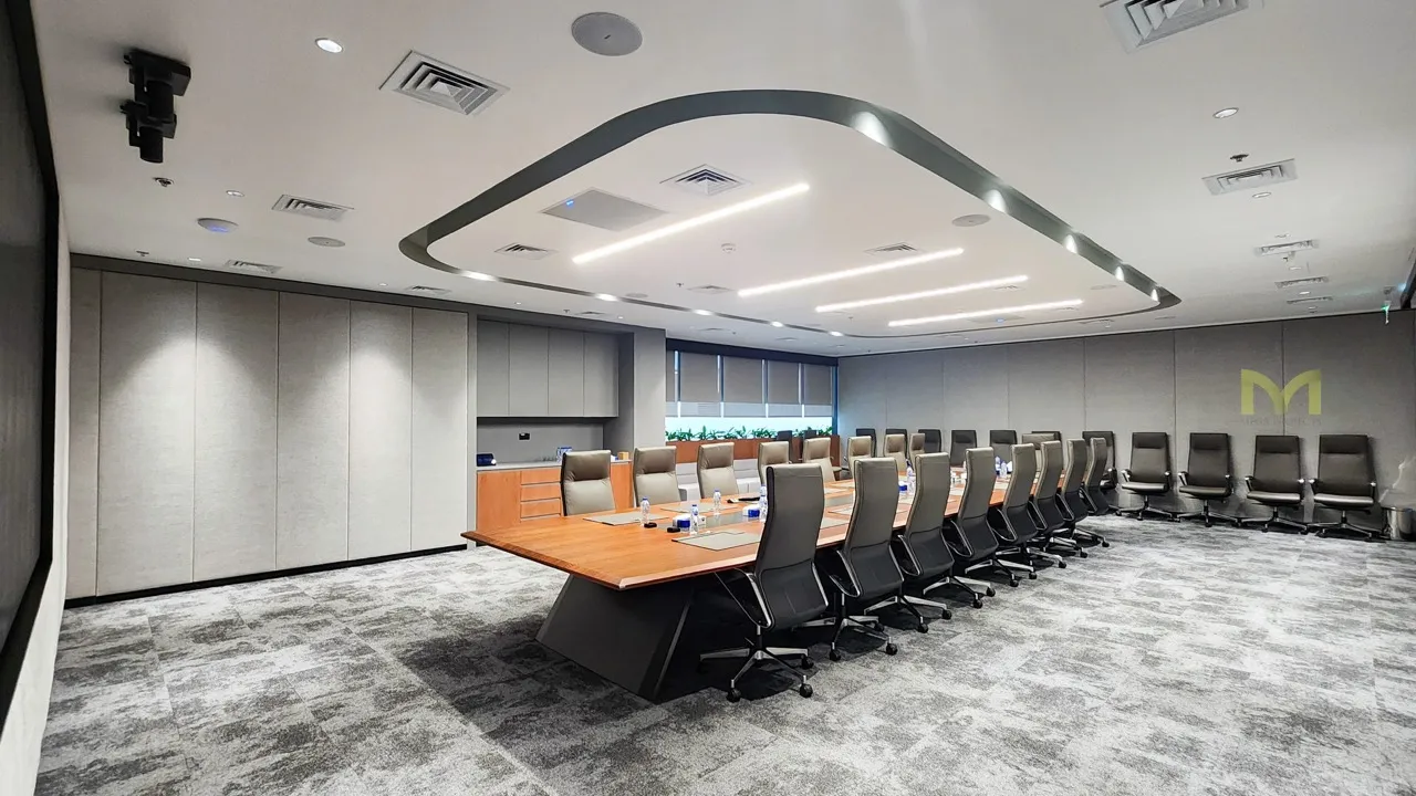 Modern conference room with a long wooden table, black office chairs, and overhead lighting.
