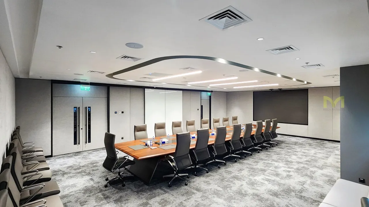 Modern conference room with long wooden table and 18 black and beige chairs on gray carpet.