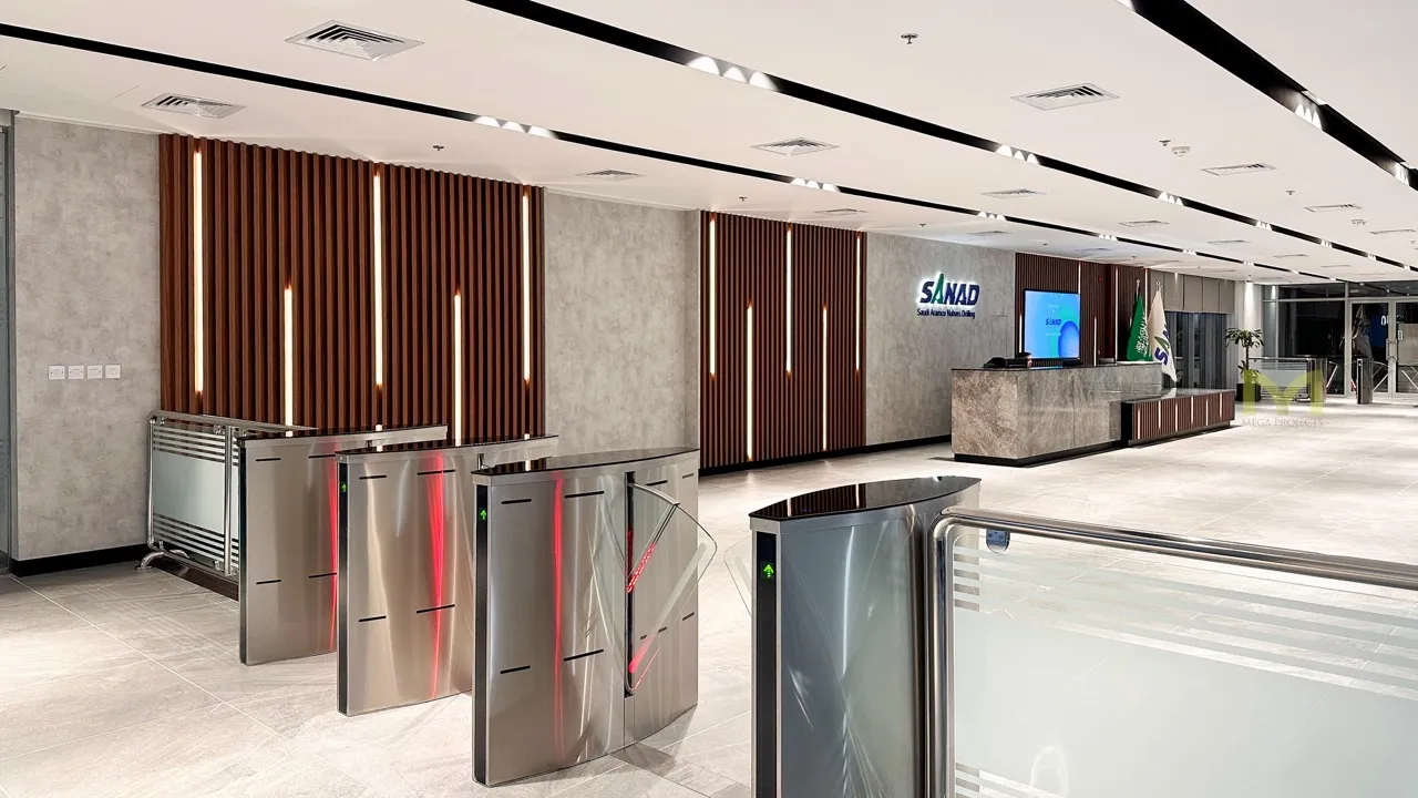 Modern office lobby with stainless steel turnstiles, a reception desk, and SANAD logo on the wall.