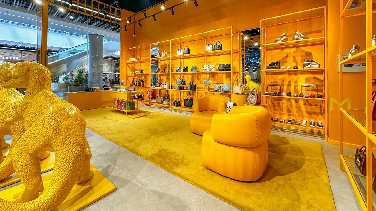 Bright yellow luxury retail store interior with leather chairs, shelves of handbags, shoes, and a yellow animal sculpture.