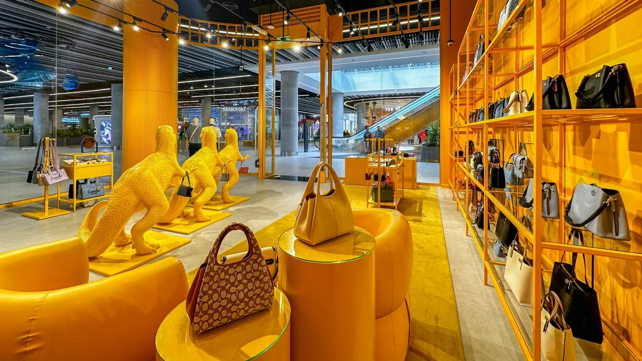 Bright yellow retail space with dinosaur sculptures and shelves displaying handbags.