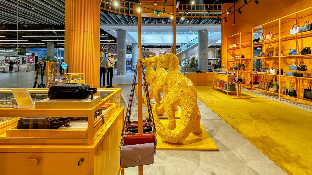Bright yellow retail store interior with dinosaur sculptures, handbags, and display cases.