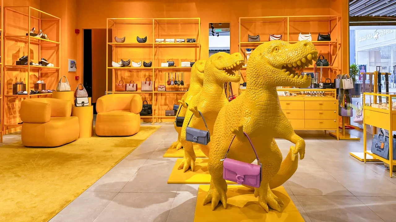 Bright yellow dinosaur statues holding handbags in an orange-themed retail store interior.